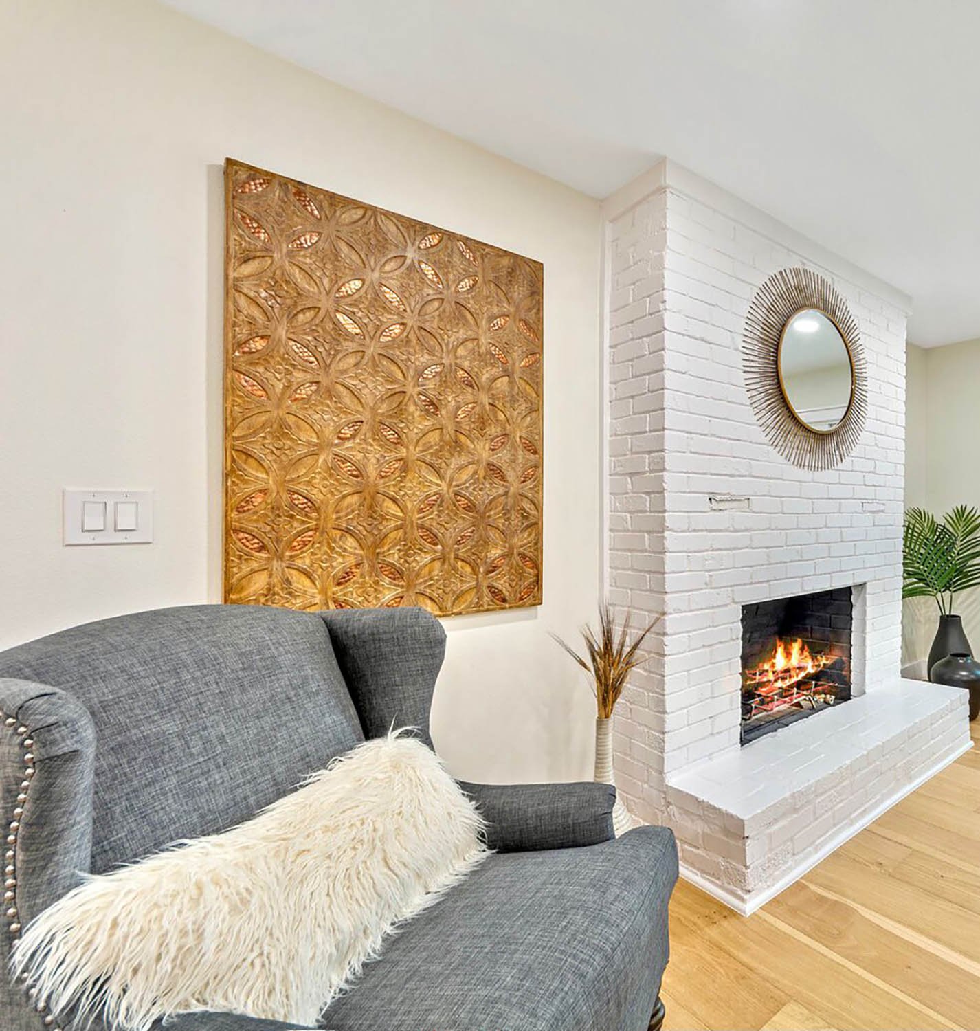 Gray wingback armchair beside a white brick fireplace with gold wall art, staged by Eleven 11 Home Staging