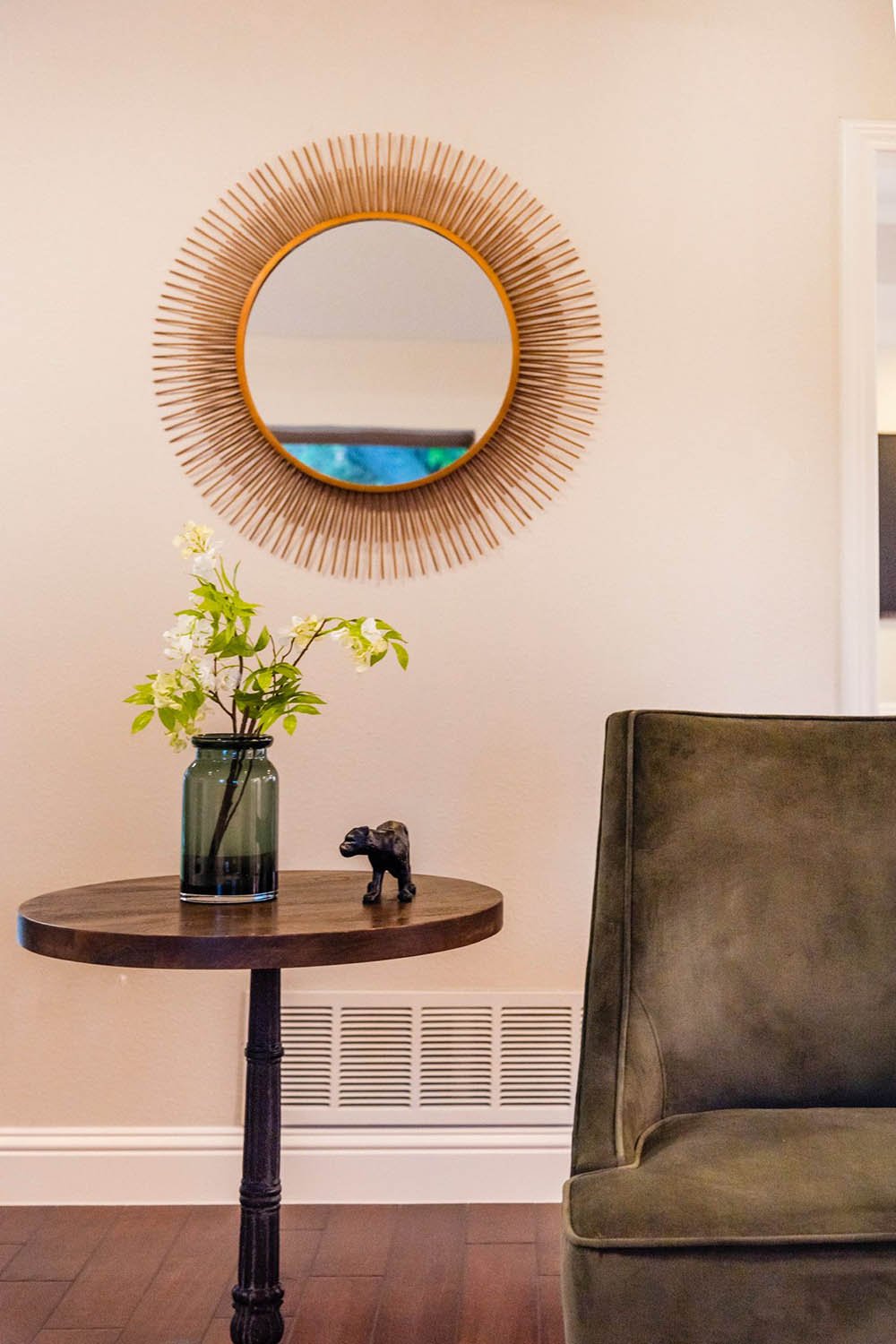 Entry vignette with a round rattan mirror and green velvet chair staged by Eleven 11 Home Staging